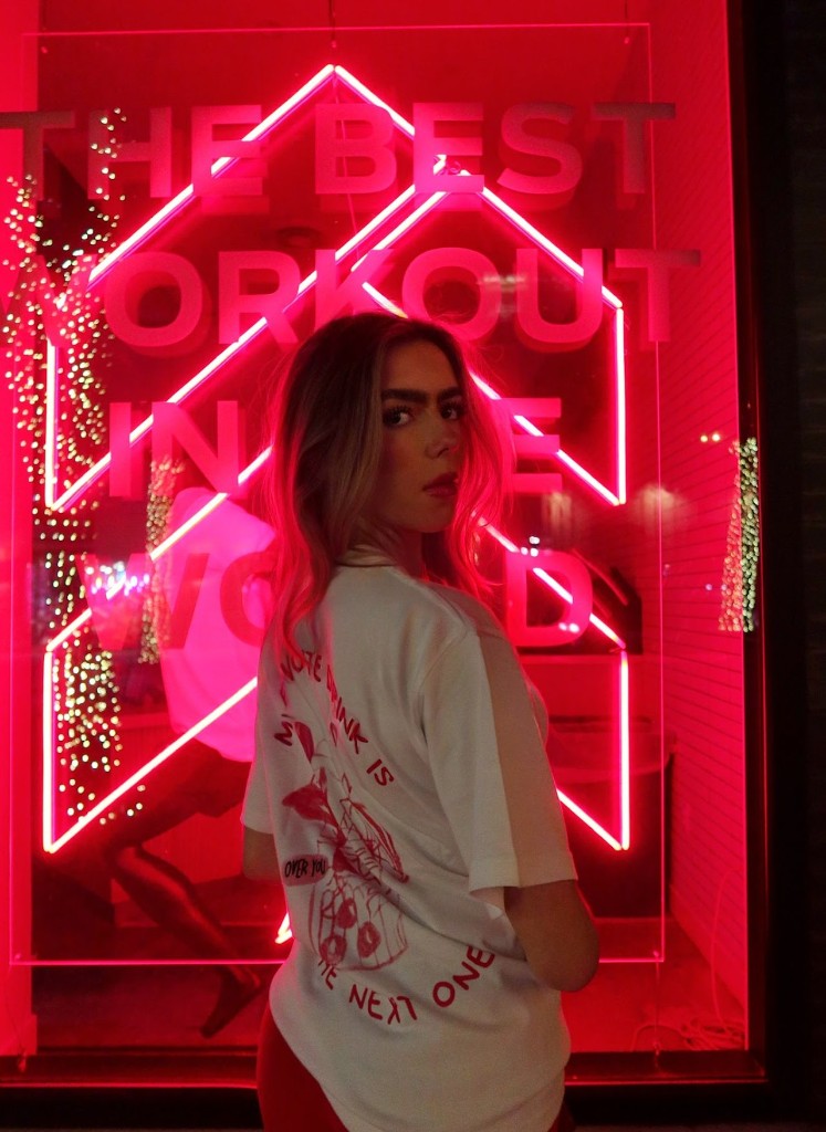 Model wearing an Over You shirt in front of a neon sign